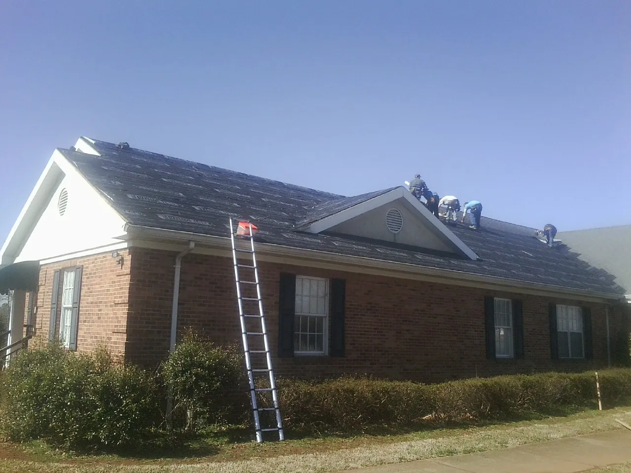 Crew tearing shingles off a brick ranch roof with a ladder set — Metal Roof Repair work by our crew in Morgantown