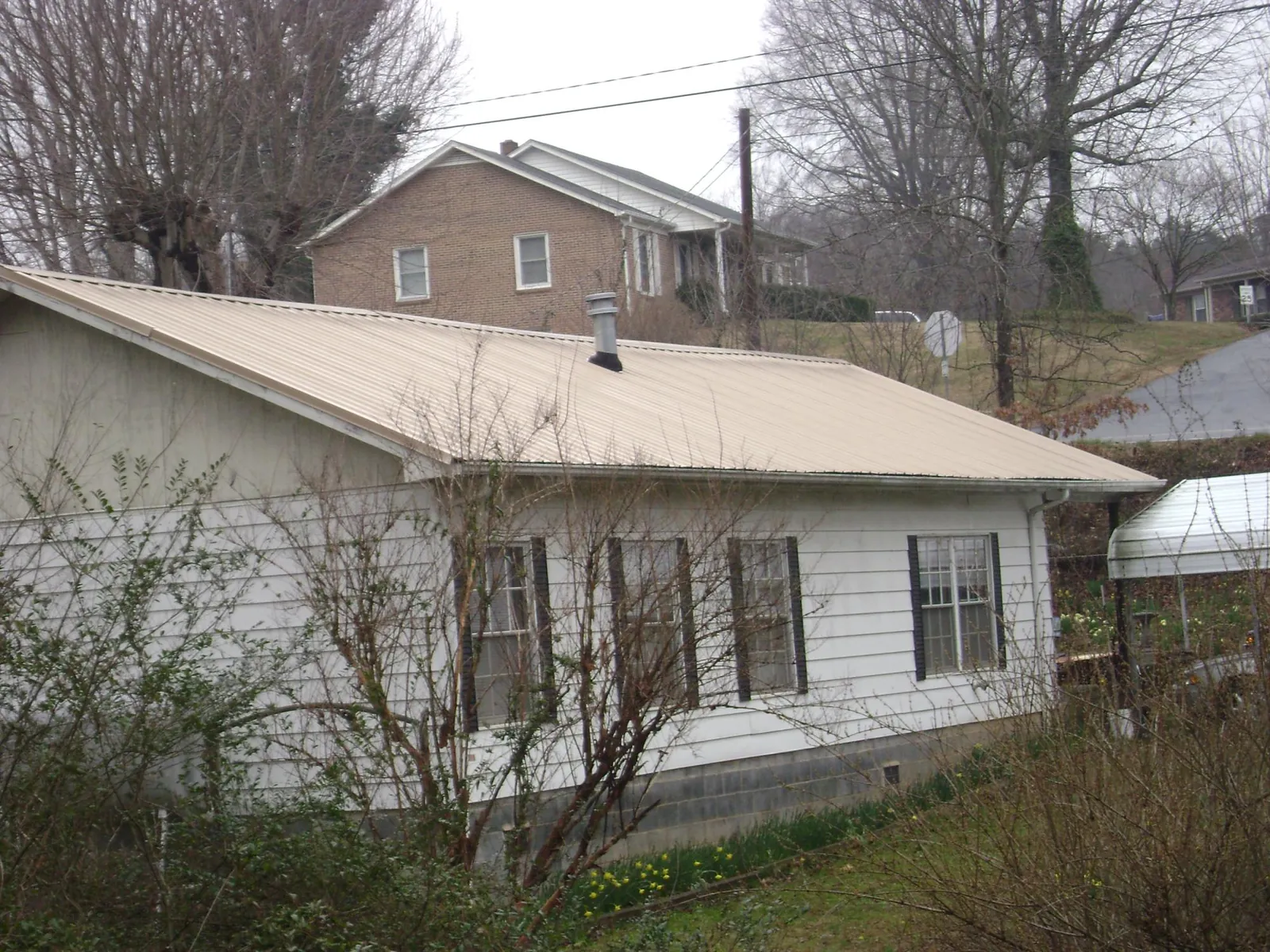 Tan metal roof on a white sided house set into a hillside — Commercial Roofing by Roofing Brothers in Morgantown